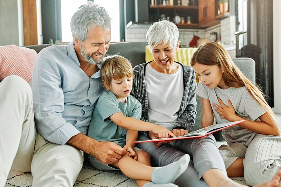 Portrait of grandparents and grandchildren having fun together reading a book at home